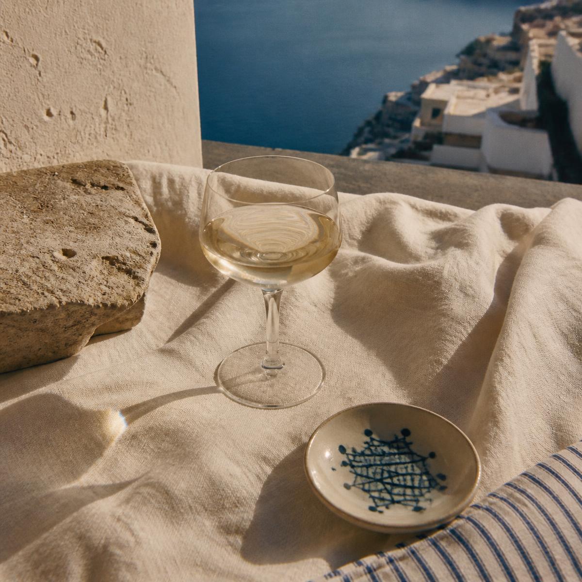 Coastal still life: cream linen, a glass of pale wine, warm stone and a ceramic dish in Mediterranean afternoon light